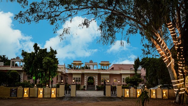 A large, multi-story building with a central entrance, surrounded by trees and illuminated by string lights. - Ranakpur Hill Resort (Desuri)