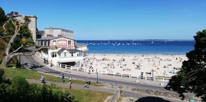A beachside building with a sign reading "Residence de la Mer" overlooking a crowded beach with numerous people and boats.