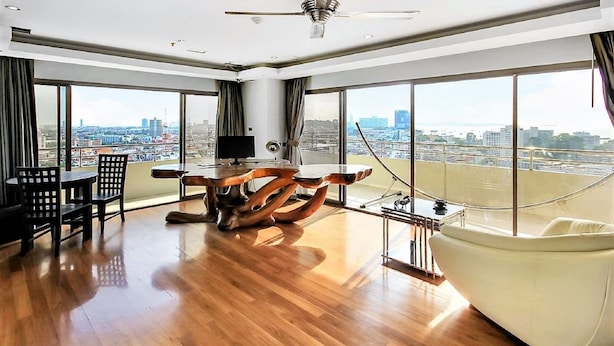 A spacious room with a large window offering a city view, a wooden coffee table, a white sofa, and a large bathtub. - 20th Floor 2-bed Condo With Stunning Views (Pattaya)