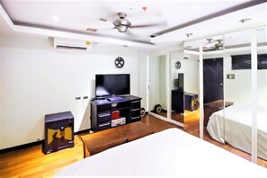 Une chambre d’hôtel moderne équipée d’un lit, d’une télévision, d’un bureau avec un ordinateur, d’un coffre-fort et d’un grand miroir.