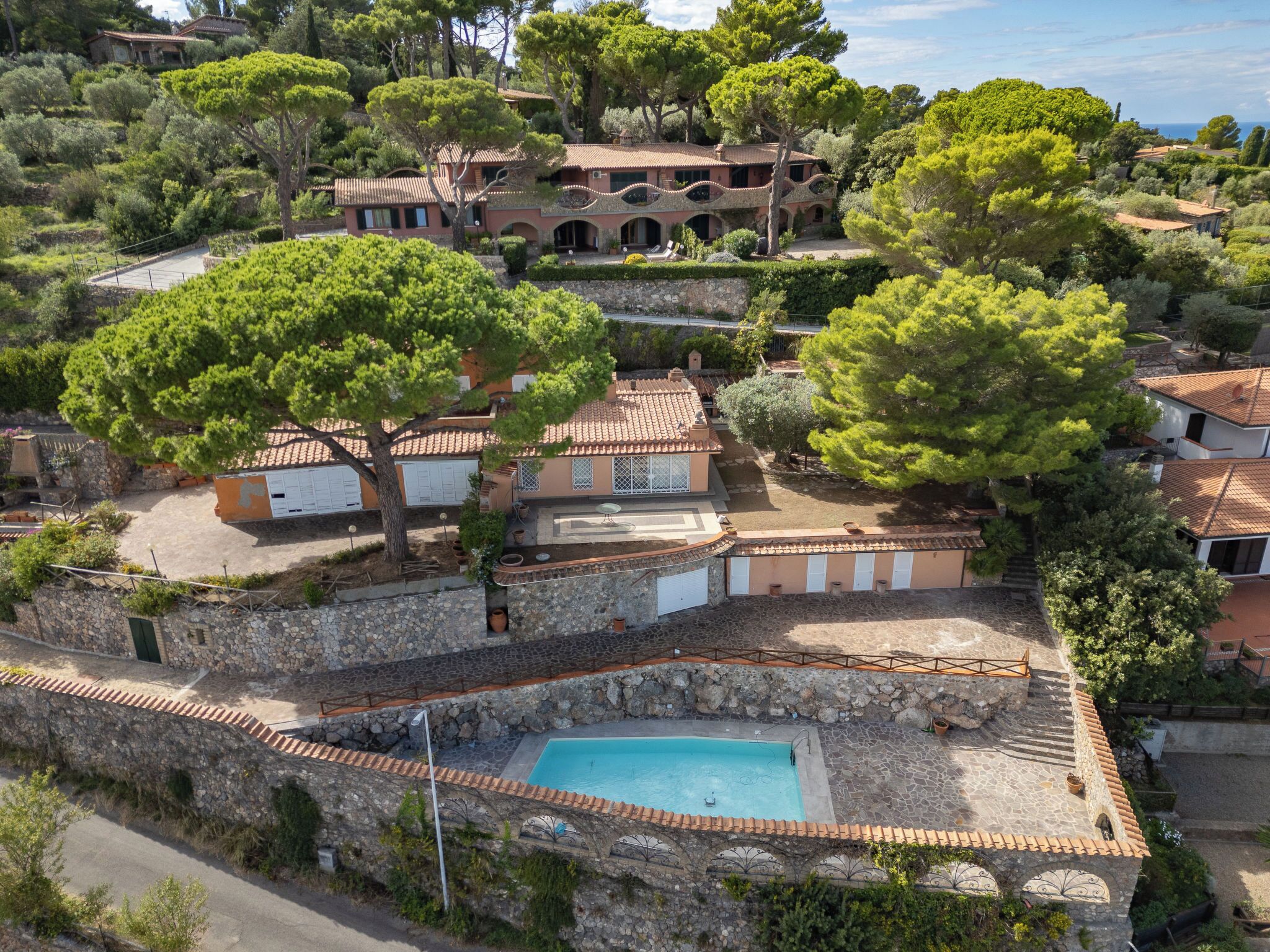 A Mediterranean-style villa with a swimming pool, stone walls, and lush greenery.