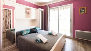 Ein Schlafzimmer mit Bett, Kleiderschrank, einem Fenster mit Vorhängen und einem Bild an der Wand.