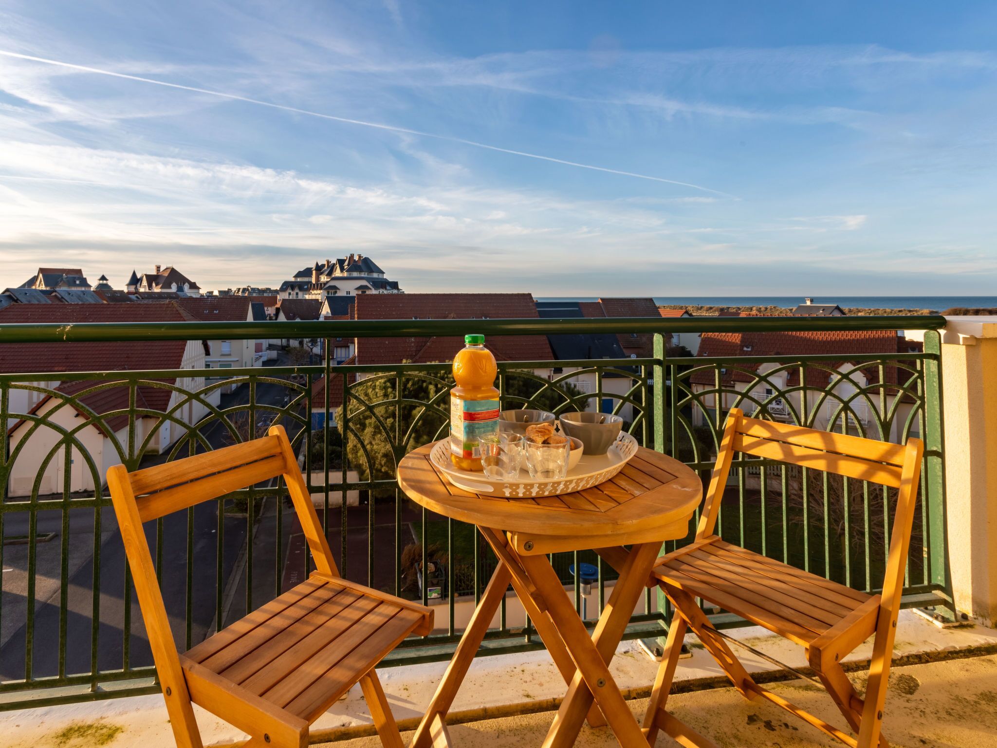 A balcony with two wooden chairs, a small round table, and a bottle of orange juice.