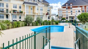 En bostadsbyggnad med en swimmingpool, omgiven av grönska och ett grönt staket.