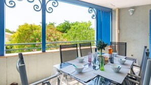 A balcony with a table set for dining, chairs, a potted plant, and a bottle of orange juice. - Terre du Soleil by Interhome (Sainte Maxime)