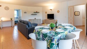A modern living room with a sofa, a dining table set for four, and a TV in the background. - Terre du Soleil by Interhome (Sainte Maxime)