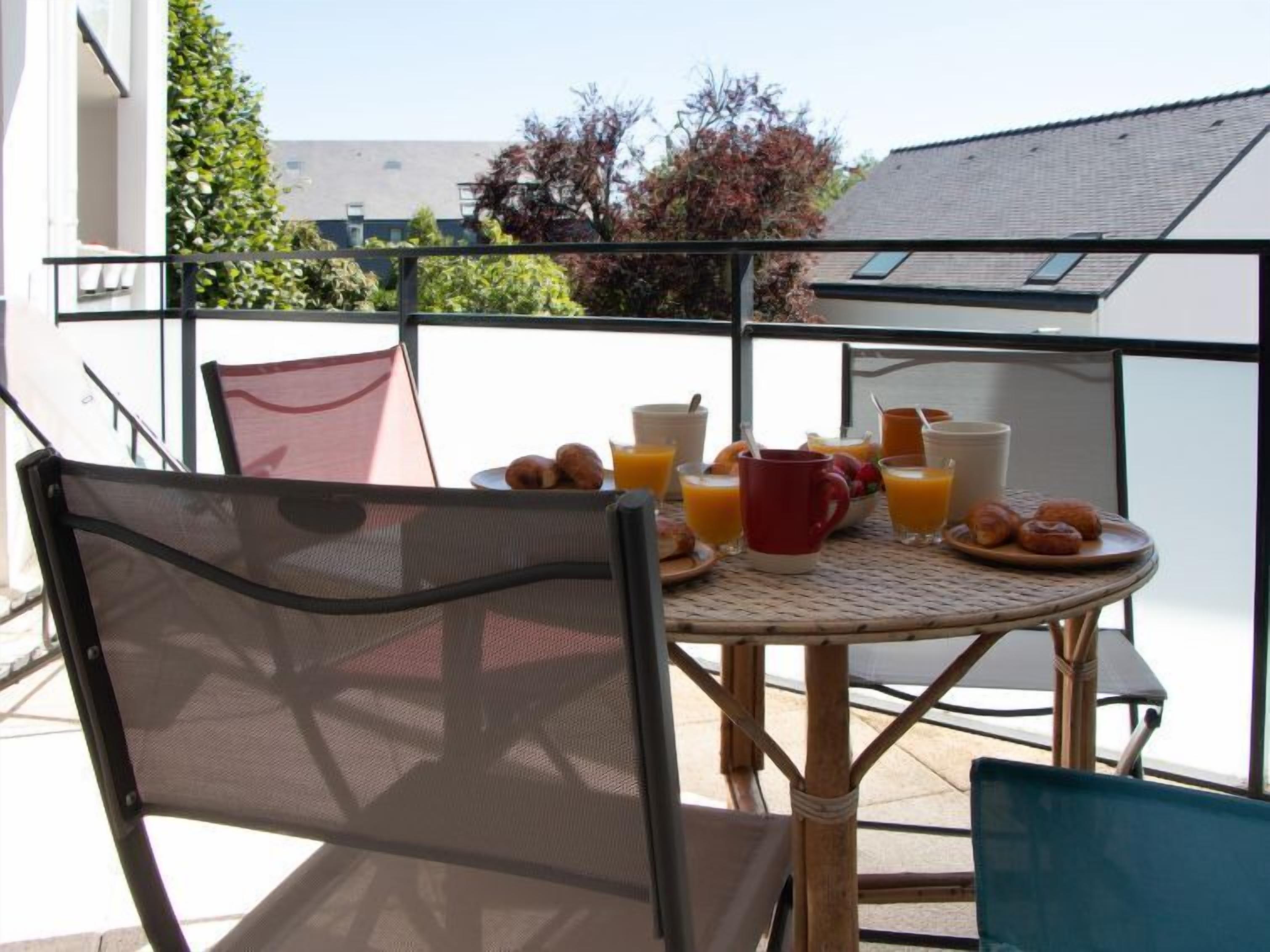 A balcony with a table set for breakfast, including croissants, fruit, and orange juice.