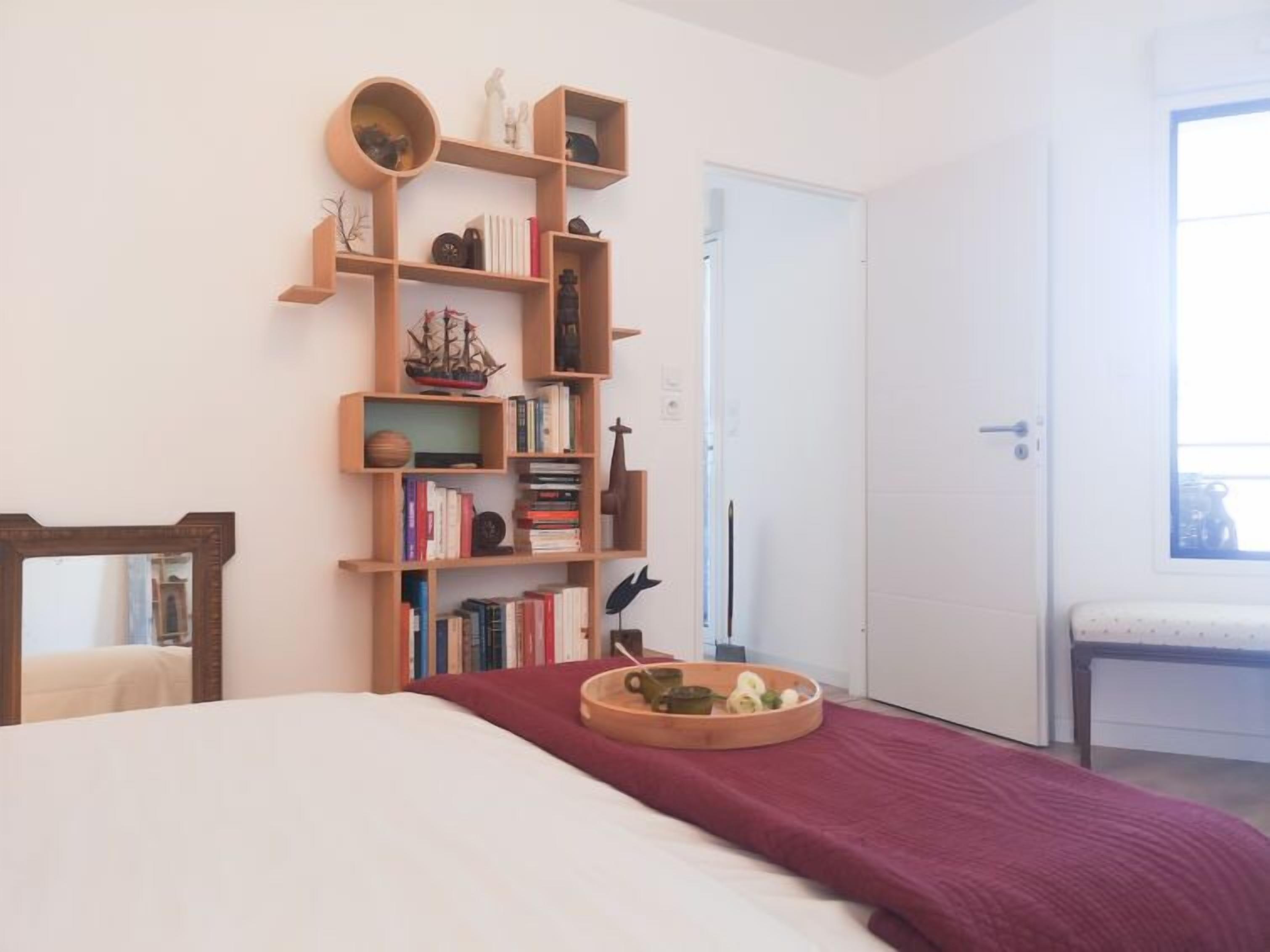 A bedroom with a large bed, a wooden bookshelf, and a small table with a tray.