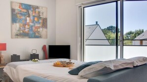 A modern bedroom with a large window, a bed with a tray of breakfast, a painting on the wall, and a TV. - Stella Marine by Interhome (Carnac)