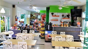 A restaurant with white chairs and tables, a counter with various food items, and a green wall with a sign. - 1 bed Condo With Direct Pool Access - Sleeps 2 (Pattaya)