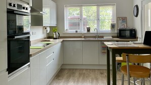 A modern kitchen with white cabinets, a built-in oven, a microwave, and a window with blinds.