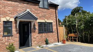 A brick house with a black door, a small garden, and a wooden bench.