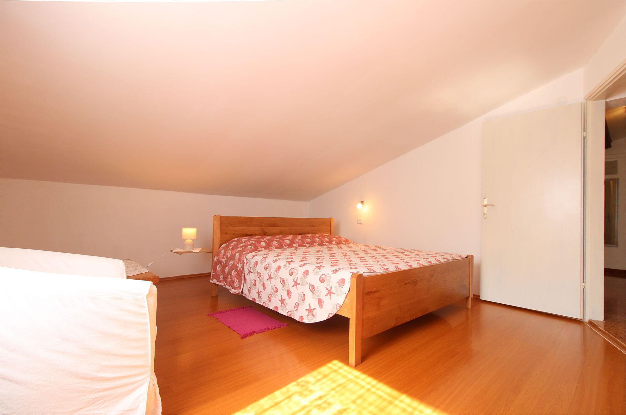 Ein Schlafzimmer mit einem hölzernen Bett, einem Nachttisch mit Lampe und einer Tür rechts.