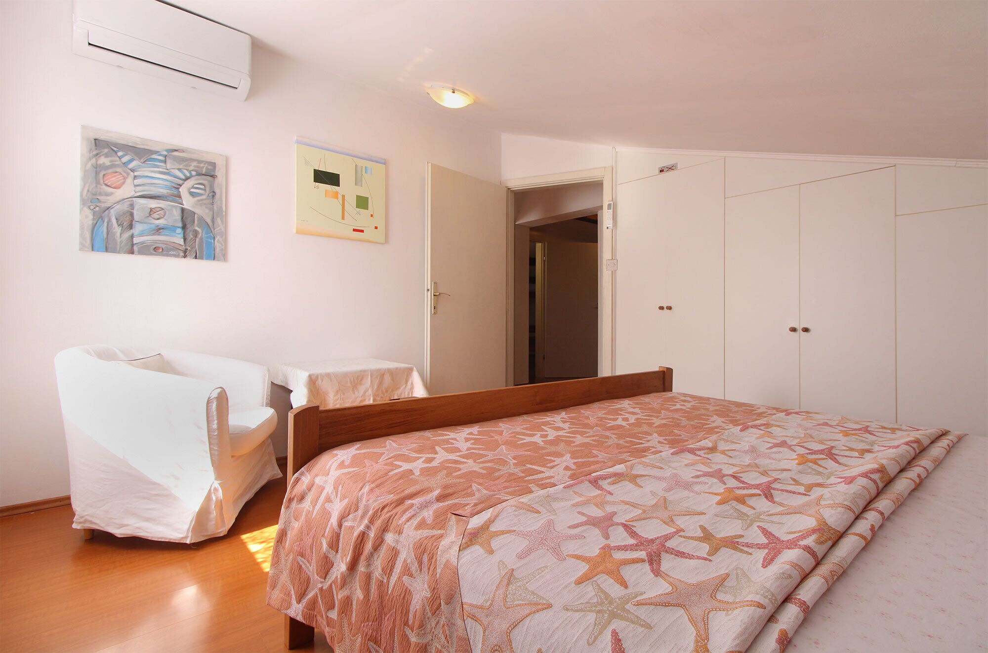 Um quarto com uma cama, uma cadeira, uma mesinha e um guarda-roupa.