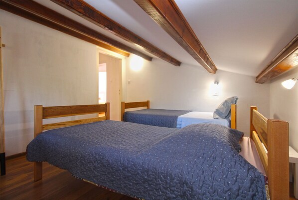 A room with two wooden beds, a wooden ceiling, and a door leading to another room.