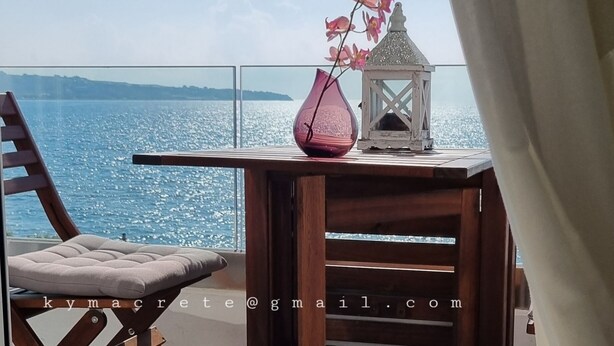 Ein Balkon mit einem Holztisch, einem gepolsterten Stuhl, einer rosa Vase und einem weißen Laternen.