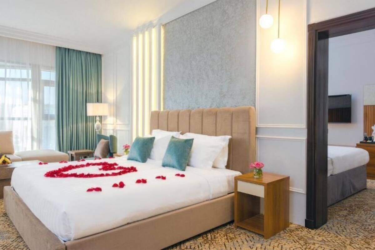A hotel room with a large bed, a bedside table, a TV, and a desk with a chair.
