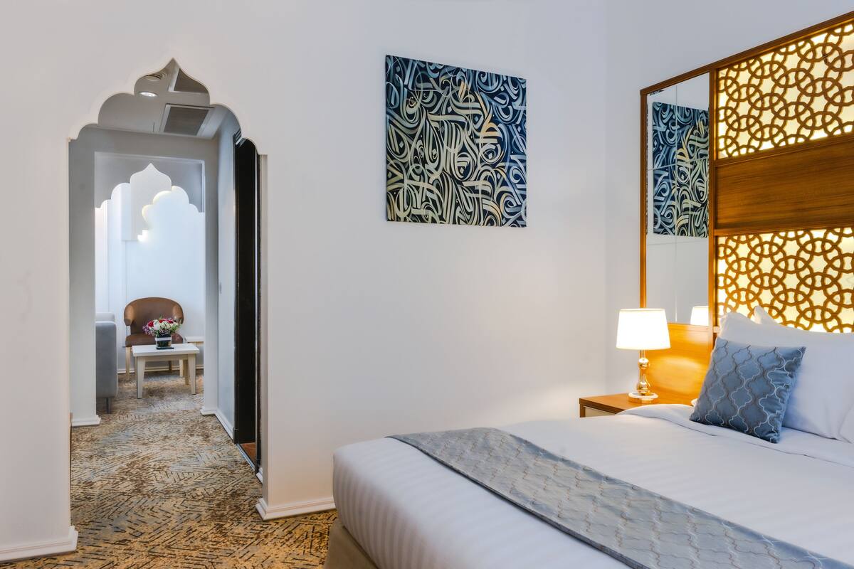 A hotel room with a bed, a nightstand, a lamp, and a decorative wall panel.
