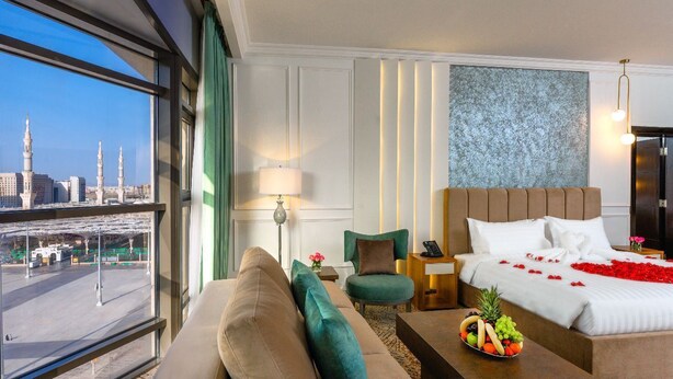Hotelkamer met een groot bed, een bank, een stoel, een tafeltje met fruit en uitzicht op een stadsgezicht met gebouwen en een brug.