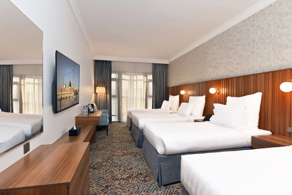 A hotel room with two beds, a wooden headboard, a large mirror, a desk, and a view of a building through the window.