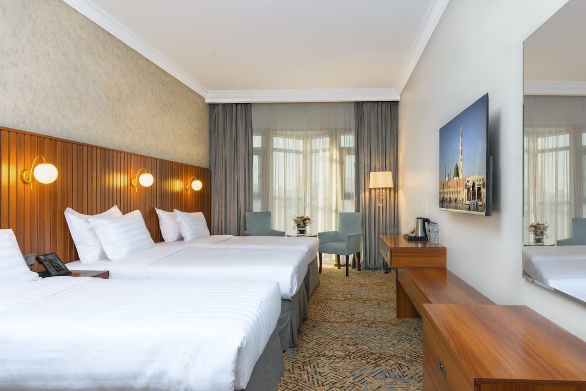 A hotel room with two beds, a desk, a chair, a lamp, and a large window with curtains.