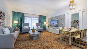 Een moderne hotelkamer met een bank, twee fauteuils, een eettafel en een televisie.