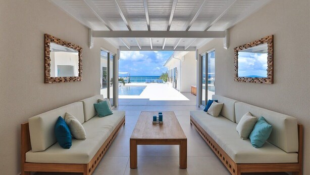 A modern living room with two sofas facing a large window, a coffee table in the center, and a view of a pool and ocean.