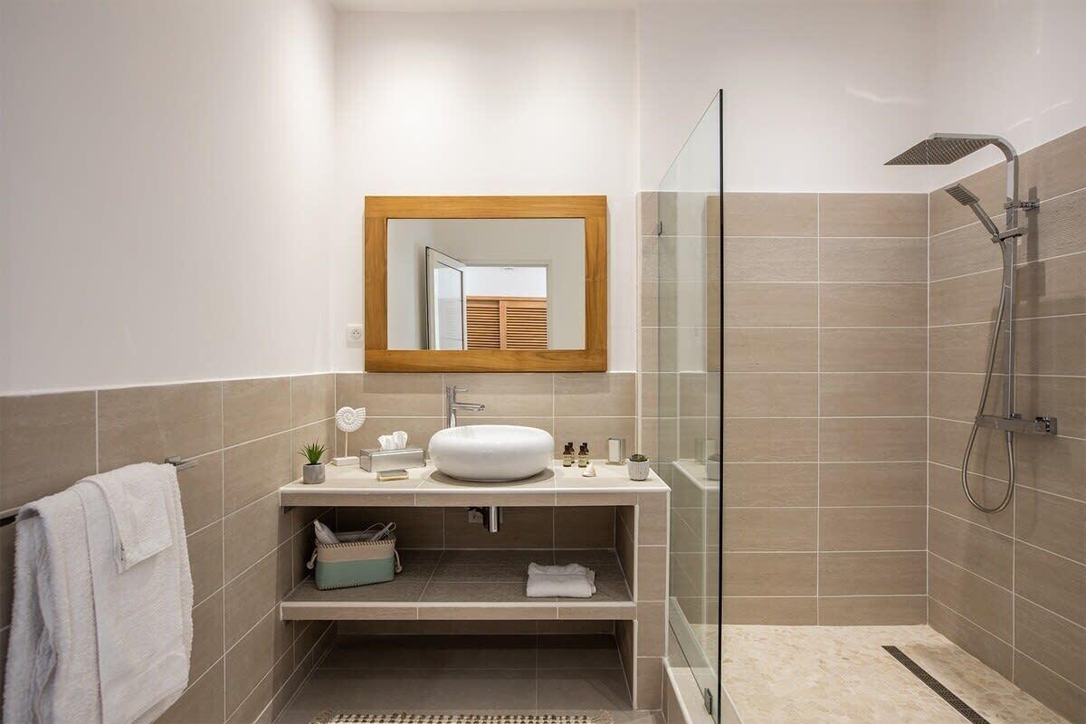 A modern bathroom with a glass shower enclosure, a wooden-framed mirror, and a vanity with a sink and storage.