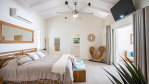 A bedroom with a bed, a ceiling fan, a TV, a mirror, and a window with curtains.