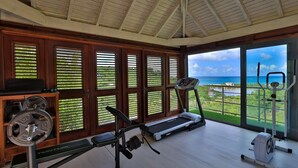 A gym with treadmills, a stationary bike, and weight machines, with large windows offering ocean views.