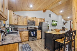 A kitchen with wooden cabinets, a microwave, a stove, a refrigerator, and a television on the wall.