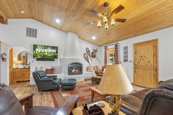 A cozy living room with a fireplace, leather furniture, and a television displaying "RED RIVER".