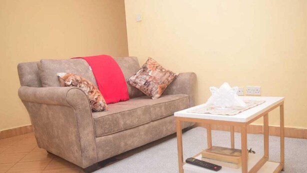 A living room with a sofa, a small wooden table, and a remote control on the table. - Stay.Plus Makey Cozy Homes (Ngong)