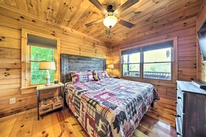 Camera da letto in una baita di legno, con un letto, due finestre, una ventola a soffitto e un comò.