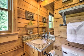 Un bagno in una baita di legno con un lavandino su un piano di granito, un water e quadri appesi alle pareti.