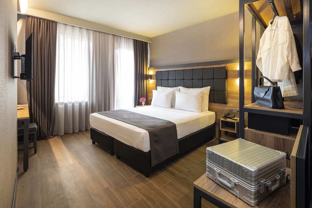 A hotel room with a bed, bedside table, desk, and a suitcase.