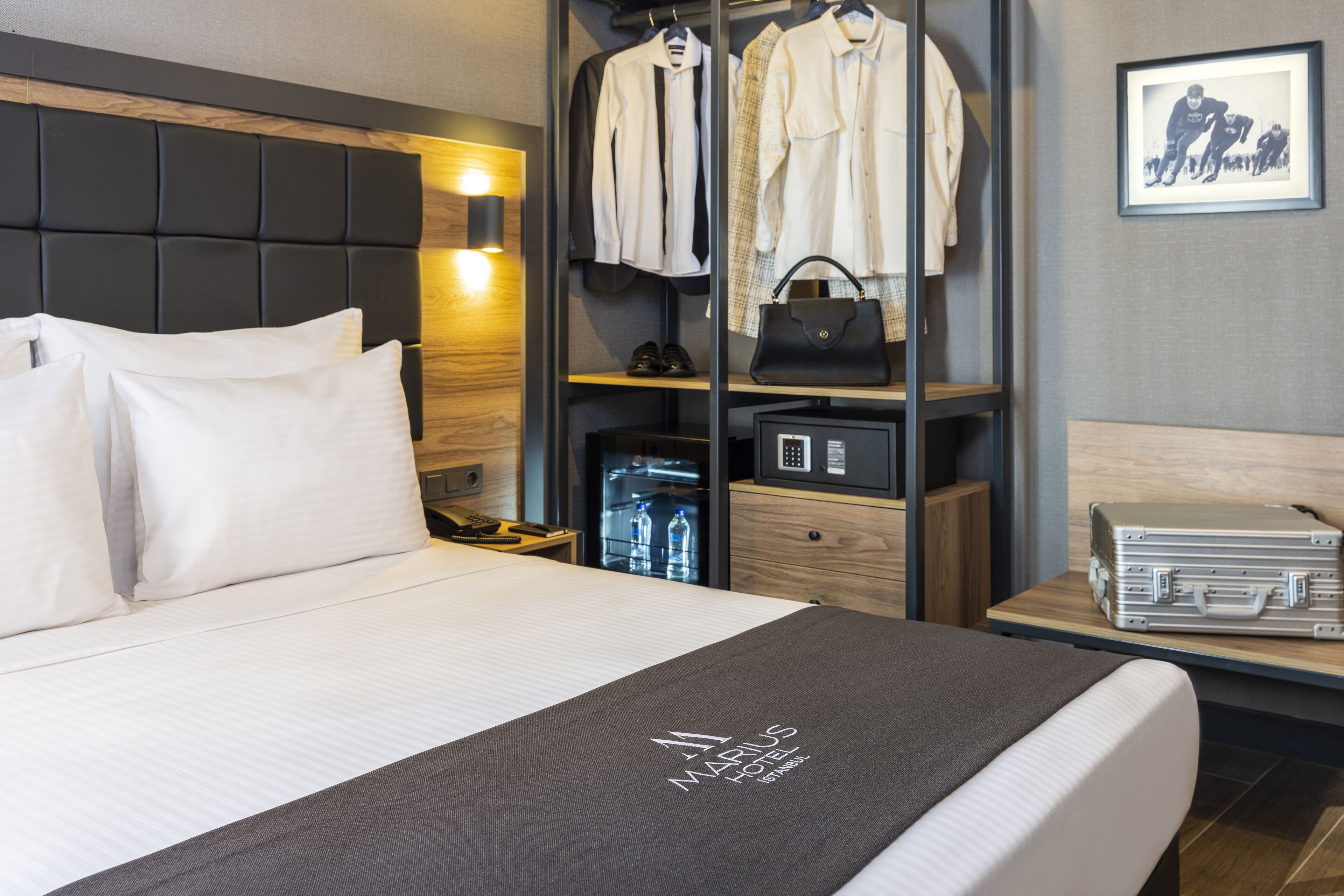 A hotel room with a bed, a wardrobe, a nightstand, and a desk with a suitcase.