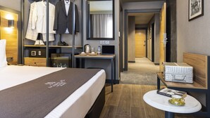 Habitación de hotel con cama, escritorio, espejo, armario y una pequeña mesa con un libro y una taza.