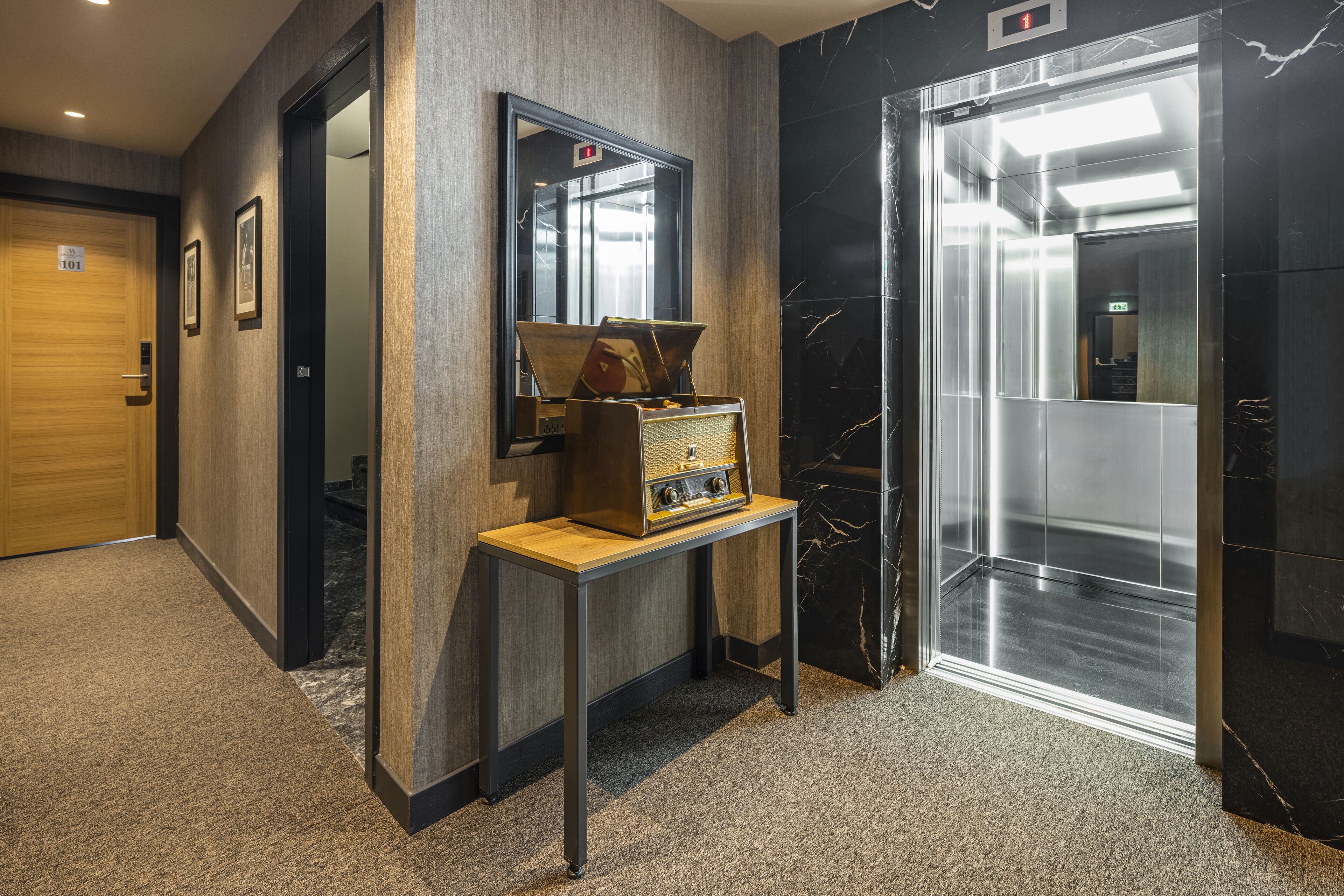 A modern elevator with a digital display, a wooden door, and a small table with a vintage radio.