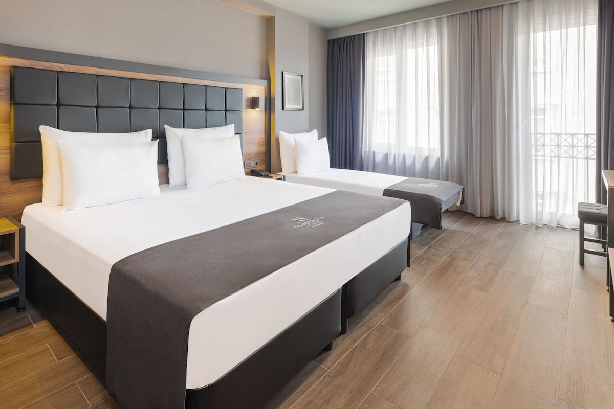 A modern hotel room with two beds, a wooden headboard, a desk, and a large window with curtains.