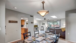 Un comedor moderno con una mesa grande dispuesta para seis personas, un ventilador de techo y vistas al área de la cocina y la sala.