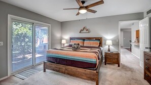 Un dormitorio con cama de madera, dos mesitas de noche, ventilador de techo y vistas a través de un ventanal corredero.
