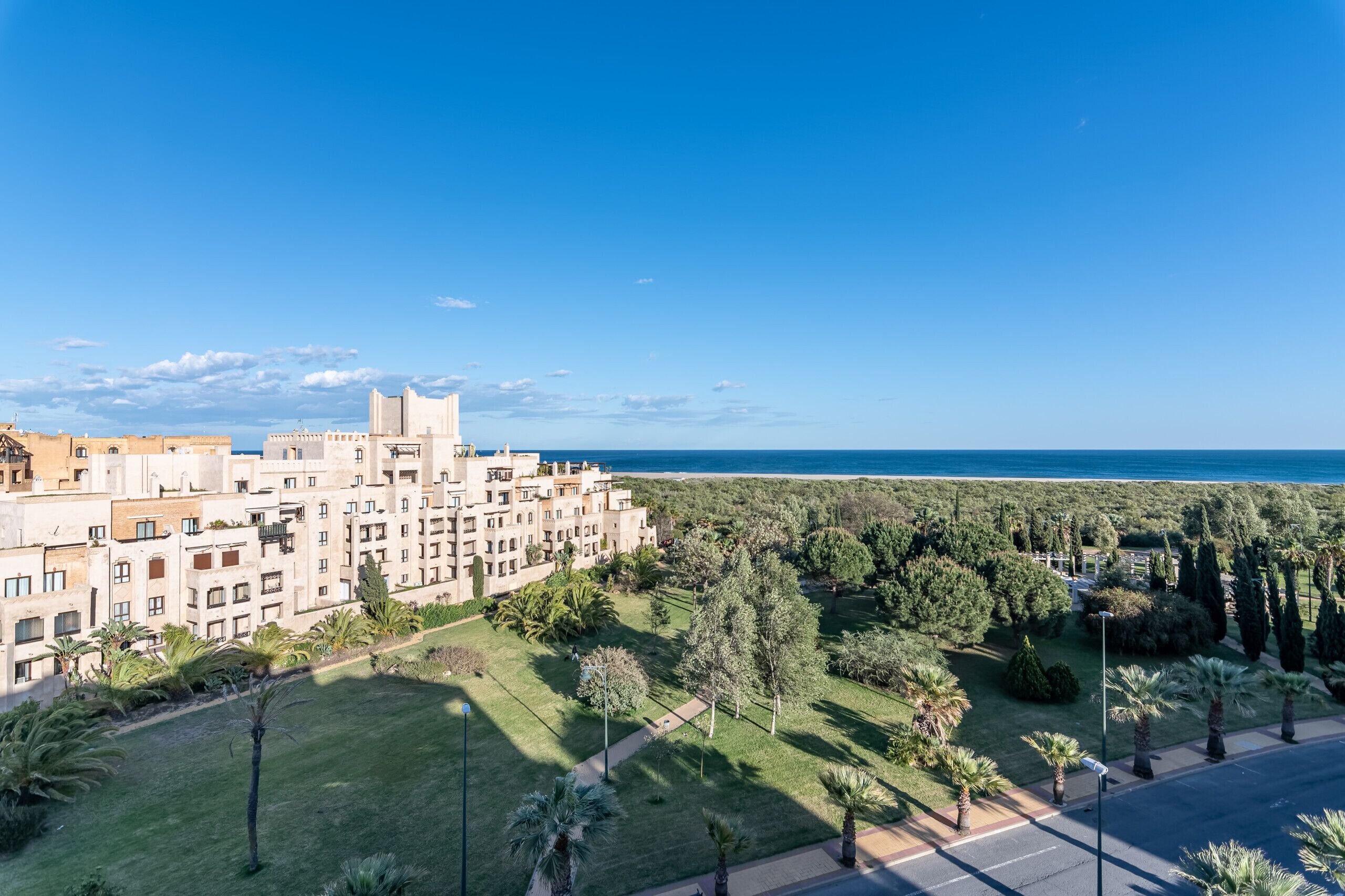 A hotel with a view of the sea, surrounded by greenery and palm trees.