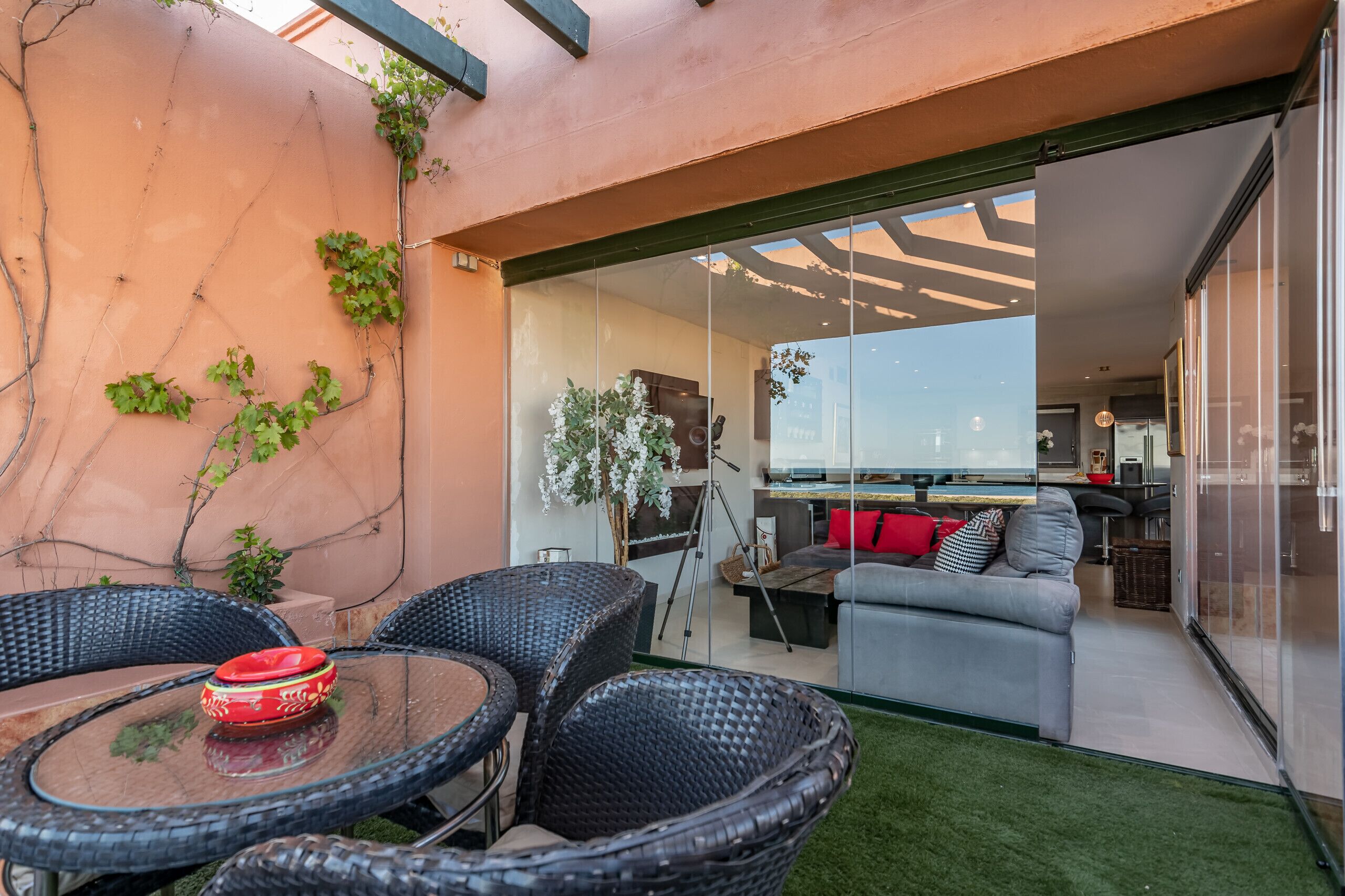 Eine moderne Außenpatio mit Korbmöbeln, einem Glastisch und einem roten Dekorationselement.