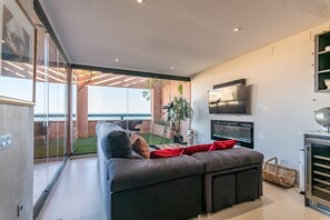 Un salon moderne avec un grand canapé, un téléviseur à écran plat et une vue sur l’extérieur.