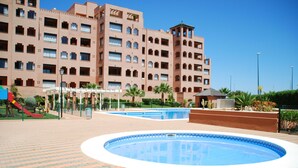 Un hotel amb diverses plantes, piscines exteriors i una zona de jocs infantils amb tobogan.