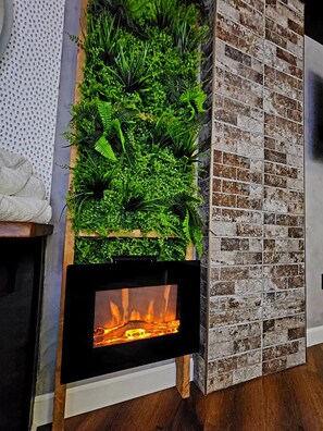 A fireplace with a fire, a vertical garden, and a brick wall.