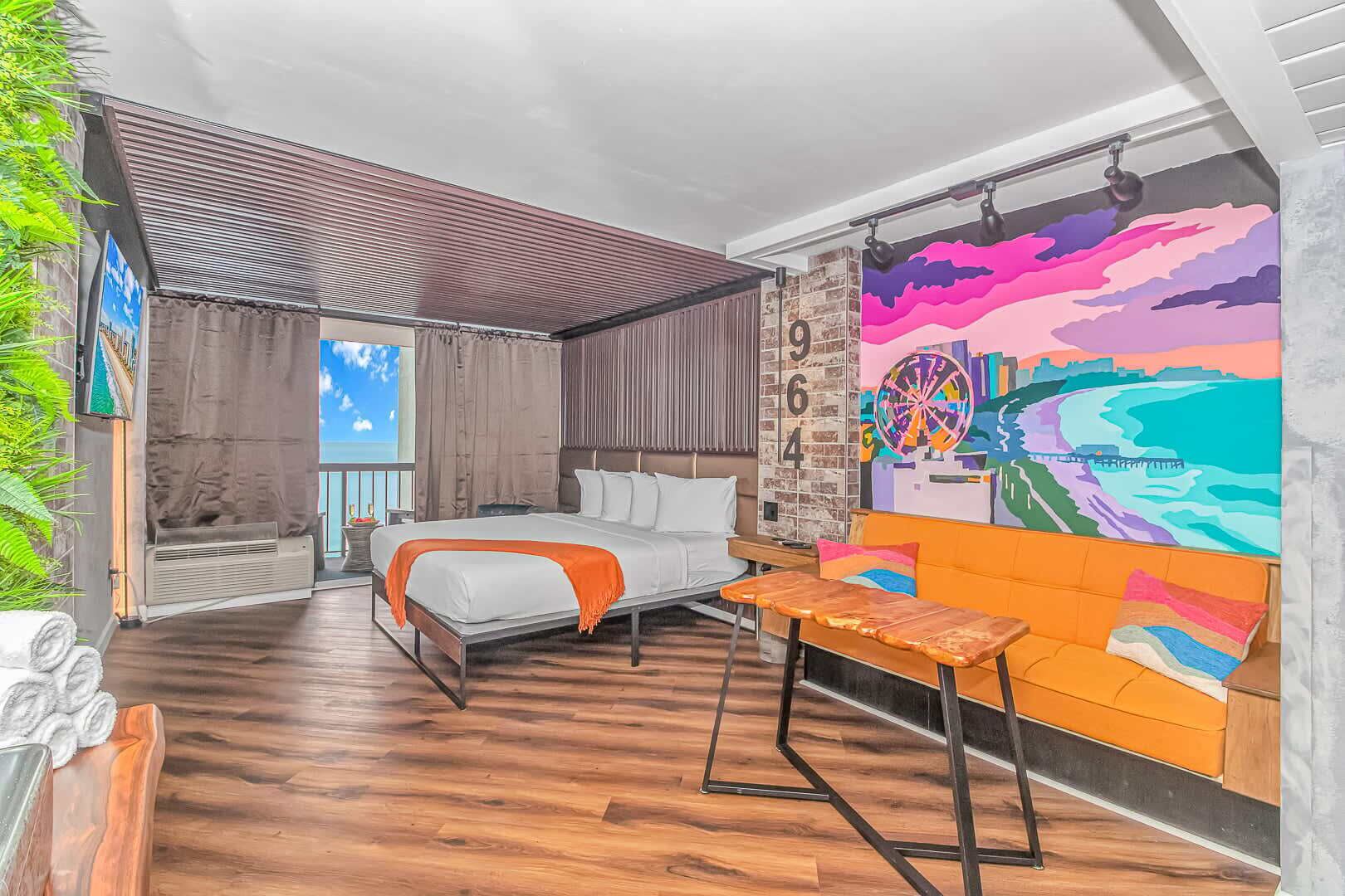 A bedroom with a bed, a sofa, a small table, a mural, and a view of the outdoors.