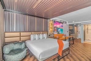 A modern hotel room with a large bed, a seating area, a dining table, and a bathroom.