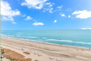 A beach with a clear sky, calm sea, and a sandy shore with a few people.